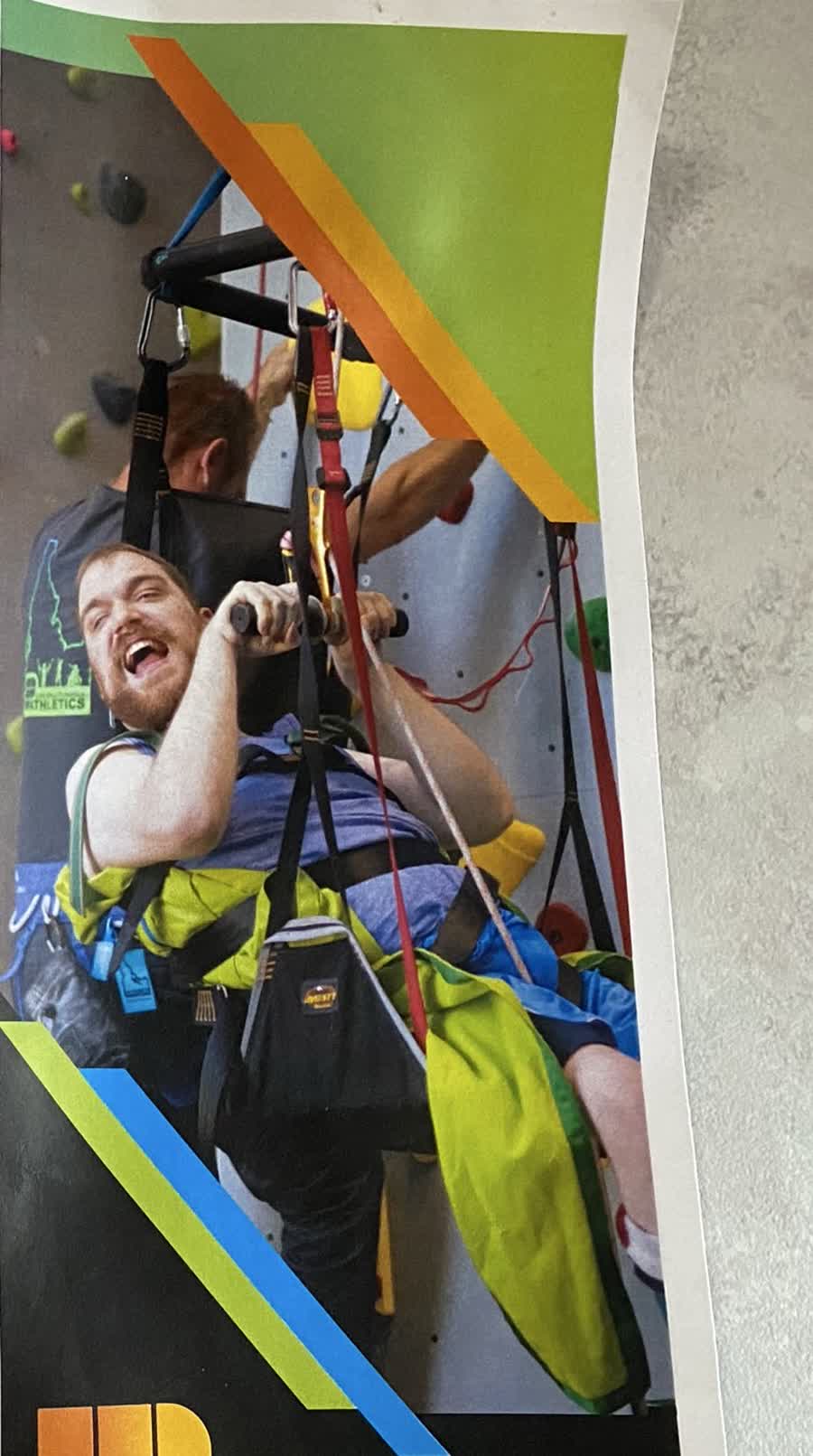 A participant smiling while using adaptive climbing equipment in a gym.